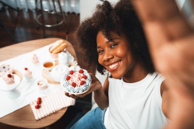 Genç ve güzel Afrikalı blogcu akıllı telefondaki selfie ile konsept özel mutfak konseptinde kek sunuyor. Favori tatlı fırın yemeğiyle sosyal medyanın yaratılması. Tatlandırıcı.
