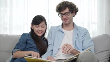 Mutlu kız babaya yaslanır hikaye anlatırken. Genç Asyalı liseli kız birlikte masal kitabı okurken ve kanepede otururken babasını arıyor. Aile eğlence konsepti. Pedagoji.