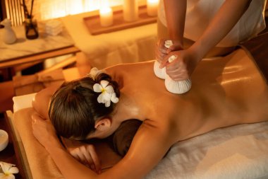 Sıcak bitkisel top spa masaj vücut tedavisi, masör kadın vücuduna nazikçe şifalı bitki torbası bastırıyor. Aromaterapi tesisinin sakinliği ve dinginliği kaplıca salonundaki mumların sıcacık ışığında. Sessiz.