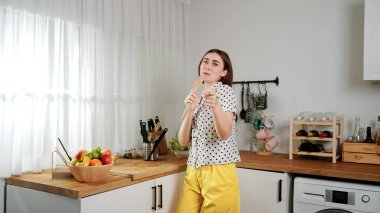 Enerjik beyaz anne kahvaltı için salata pişirirken ve yemek pişirirken elinde kepçeyle şarkı söylüyor. Sağlıklı yemek yapmaya hazırlanırken müziğe yönelen mutlu ev sahibi. Pedagoji.