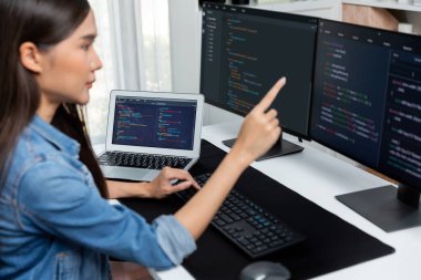 İnternet sitesinde kodlama programı uygulaması olan ve kot gömlek giyen bilgisayar hakkında bilgi veren IT geliştiricisi genç bir Asyalı kız. Güvenlik programlarıyla çevrili iki ekran. Taktik.