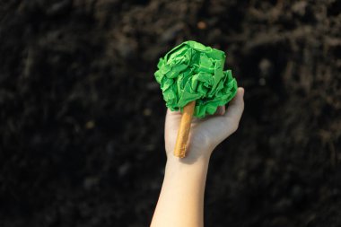 Çocuk, gübrelenmiş toprağı, sürdürülebilir ekoloji ve ormanlaşmalı daha yeşil çevre için büyüyen ve besleyen bitki konseptinin bir parçası olarak kağıt ağacı tutuyor. Döngü