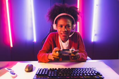 Oyun flamasının sunucu kanalı, joystick ile online oyun oynayan Afrikalı kız, mikrofondan izleyici medyasıyla konuşuyor. Esport yetenekli takım oyuncuları neon renkli aydınlatma odasında. Tatlandırıcı.