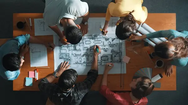 从上往下看土木工程师小组在设计图上用彩色调色板在会议桌边书写 由不同的人组成的小组在经理查看项目计划时进行规划和记录 专题讨论会 — 图库照片