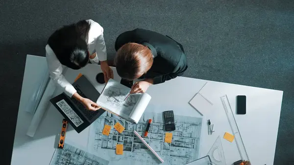 Top view of businesswoman hand blueprint to engineer sitting at meeting table with project plan, equipment and safety helmet. Aerial view of manager explain about building construction. Alimentation.