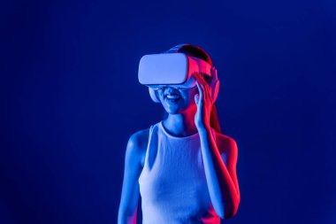 Siberpunk neon ışıklı cihazlarla çevrili zeki bir kadın metaevrene bağlı VR kulaklık takıyor, gelecekçi siber uzay teknolojisi. Zarif bir kadın sanal ortamda yaratılmış gibi görünür. Halüsinasyon.