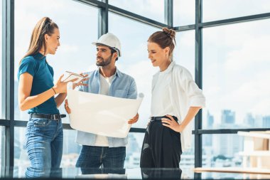 Bir grup mimar mühendis proje planına bakarken, yapı hakkında beyin fırtınası yapıyorlar. İdari ekip inşaat hakkında şehir manzaralı bir yerde dururken tartışıyor. İzleme.