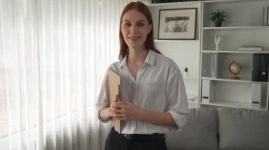 Klinikteki dost canlısı psikolog kadın. Profesyonel portresi. Kameraya bakıp psikolog muayenehanesine bakıyor. Tecrübeli ve kendinden emin psikolog.