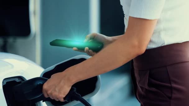 현대적인 라이프 스타일 여성은 충전소에서 자동차에 충전기를 삽입하고 스마트 폰에서 — 비디오