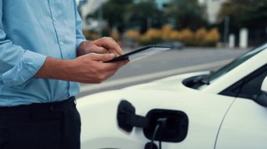 Modern iş adamı akıllı telefonun 3D hologramından batarya durumunu kontrol ederken EV arabasının şarj olan enerjisini kontrol ediyor. Gelecekteki EV otomotiv teknolojisinin yenilikçi teknolojik gelişimi. İnceleyin