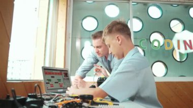 Akıllı öğrenci kodlama programı ve araba modelinden yetenekli öğretmene. Genç, elektronik ekipmanların etrafa saçıldığı masadaki robot makineler için bilgisayar kullanıyor. Öğretim