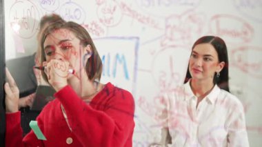 Başarılı proje yöneticisi fikrini cam tahtaya sunup yazarken aynı zamanda meslektaşına yaratıcı iş toplantılarında pazarlama stratejisini soruyor. Birlikte çalışmak, beyin fırtınası yapmak. Tertemiz..