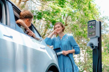 Elektrikli araçla aile gezisi, anne ve oğlu EV 'yi yeşil ve temiz enerjiyle şarj ediyor. Sürdürülebilir çevre için doğa ve çevre dostu arabayla seyahat. Kalıcı