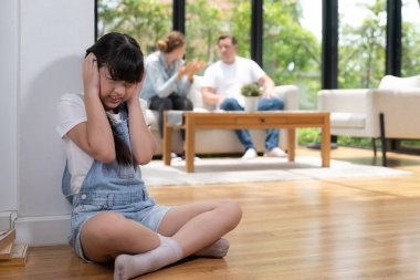 Stresli ve mutsuz kız köşede toplanır, ailesi arka planda tartışırken kulaklarını acılı bir ifadeyle kapatır. Aile içi şiddet ve travmatik çocukluk depresyona dönüşür. Eşzamanlama
