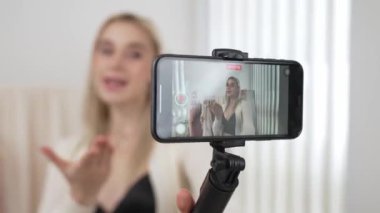 Genç sosyal medyum kadın selfie çubuğuyla moda videosu yapıyor. Blogcu kameraya gülümserken çevrimiçi kıyafetleri izleyicilere ya da takipçilere vlog sattırıyor. Blithe