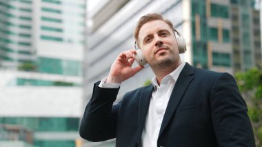 Erkek liderin etrafını sarın kulaklığı dinleyin ve neşeli ve motive edici bir şekilde rahatlatıcı müzikle dans edin. Becerikli proje yöneticisi şehir merkezinde akıllı telefon kullanırken rahat şarkılar dinlemeyi sever. Urbane.