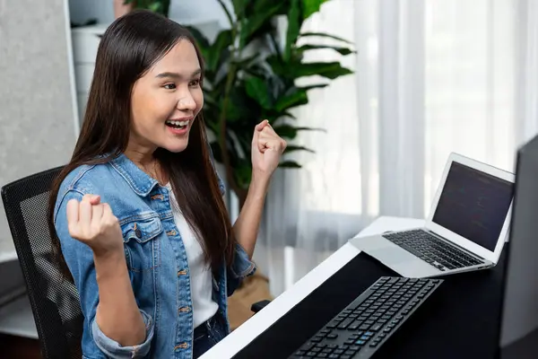 Smiling young Asian IT developer with happy face getting new software development information project with customer looking on pc screens, creating program coding to test at home office. Stratagem.