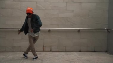 Asyalı akıllı hipster, kulaklık ve şık kıyafetler giyip hip hop şarkıları dinlerken gri arka planlı enerjik break dans gösterisi yapıyor. Açık hava sporu 2024. Hip hop hareketi. Yumuşak bir şekilde..