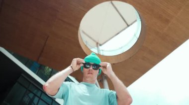 Beyaz tenli yakışıklı hipsterin güneş gözlüğü takıp kameraya bakışının düşük açılı portresi. Serbest stil dansı yaparken ve kameraya poz verirken şık bir dansçı gülümsemesi. Açık hava sporu 2024 hiphop..