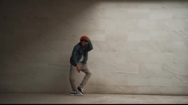 Profesyonel Asyalı hipster gri arka planda break dans yapıyor. Sokak dansçısı hip hop dansı yaparken şık bir hip hop kıyafeti giyer ve funky müzik eşliğinde dans eder. Açık hava sporu 2024. Yumuşak bir şekilde..