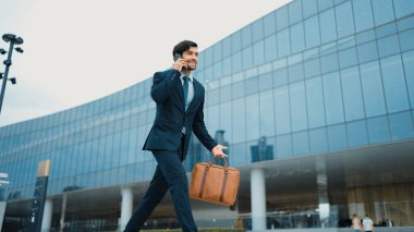 Akıllı iş adamı binada yürürken telefonla konuşuyor. İş planı, pazarlama stratejisi ya da çalışma hakkında konuşmak için akıllı telefonla konuşurken sokakta yürüyen mutlu bir yönetici. Sevinçli..