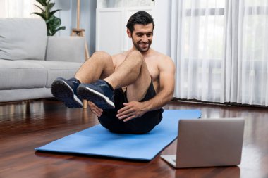 Atletik ve sporcu adam spor paspası üzerinde çatırdarken evdeki formda fiziğe ve sağlıklı spor yaşam tarzına uygun online ev eğitimi takip ediyor. Çevrimiçi neşeli ev egzersizi videosu.