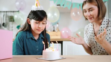 Energetic daughter and mother singing birthday song while clapping hand to music together. Caucasian mom celebrated birthday while using cake at dinning room decorated with colorful balloon. Pedagogy. clipart