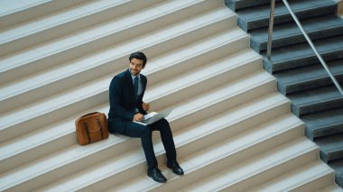 Merdivenlerde dizüstü bilgisayar kullanarak yatırımcıların çalışma ya da planlama stratejisinin en üst görüntüsü. Modern bir otelde dizüstü bilgisayar kullanarak veri analizi yapan takım elbiseli profesyonel bir iş adamı. Sevinçli..