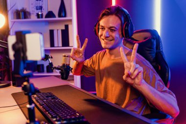 Oyun kanalı, online oyun oynayan akıllı flamalı oyun sunucusu, kulaklık takan, neon ışıklandırma odasındaki takım oyuncusuyla akıllı telefondan canlı yayında konuşan izleyiciler. Bireysel.