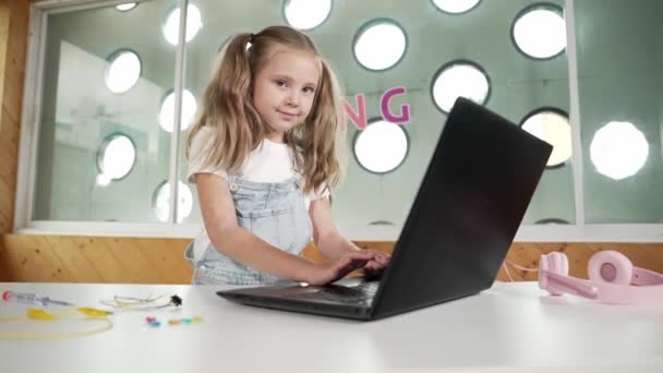 宿題をすることに集中しながら ラップトップに取り組んでいる白人少女 タイピングやゲームをしながらラップトップ画面を見ている学生 子供はテーブルの上に置かれたロボットが付いているオンライン教室に出席します エラー — ストック動画