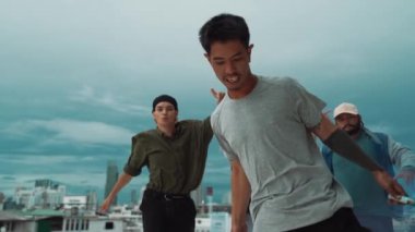 Bir grup çok kültürlü hippi çatıda işaret fişeği çalıyor. Zenci dumanı tutan çekici bir sokak dansçısı hip-hop müzik eşliğinde break dans yapıyor. Açık hava sporu 2024. Sokak dansı. hiphop.