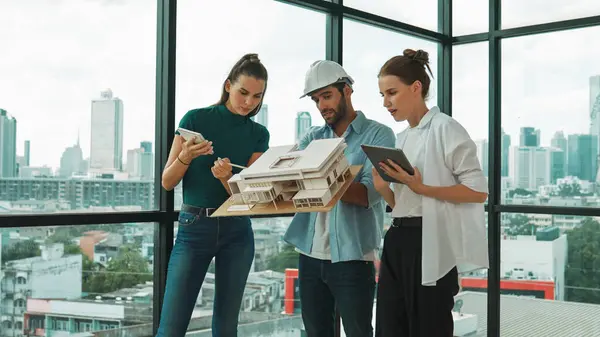 Skilled engineer holds house model and explain about house construction to skilled manager. Group of interior designer inspect architectural model. Working together, Civil engineering. Tracery