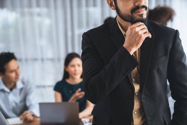 İş adamı, toplantı odasının arka planında çeşitli iş arkadaşlarıyla güven içinde poz veriyor. Çok kültürlü ekip iş başarısı için birlikte çalışır. Modern iş adamı portresi. Uyum