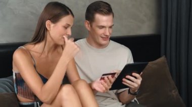 Genç çift, kredi kartıyla ödeme yapabilmek için internet üzerinden ödeme uygulaması ve dijital cüzdan kullanarak yatak odasında oturuyor. Mobil internet üzerinden alışveriş ve modern alımlar. Düzenle