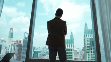 Arkaya bakan hırslı işadamı süslü bir ofiste dikilip şehir manzarası siluetine bakıyor. Kararlılık ve iş hırsı iş kariyerini parlak bir geleceğe taşıdı