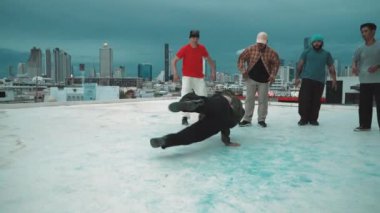 Profesyonel hippi hareketsiz poz verirken aynı zamanda şehir manzaralı çatıdaki müziğe ayak basıyor. Break dansçı, hip-hop dansçıları grubuyla birlikte sokak dansı yapıyor. Açık hava sporu 2024 hiphop..