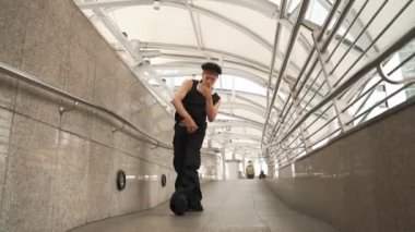 Yakışıklı hippi dar koridorda sokak dansı yapıyor. Profesyonel hip-hop dansçısı şık kıyafetler giyerken B-boy 'un şehir koridorunda yürüdüğünü gösteriyor. Açık hava sporu 2024. Yumuşak bir şekilde..
