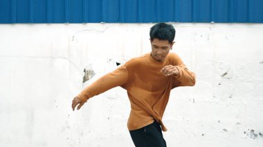 İspanyol adam kollarını açıp duvarın önünde dans ediyor. Modern bir sokak dansçısının, günlük kıyafetleriyle hip hop tarzında dans ederken çekilmiş bir fotoğrafı. Açık hava sporu 2023. Geçmişi. ÇalışmaComment.