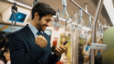 Profesyonel iş adamı trende dururken terfi aldığı için kutlama yapıyor. Beyaz erkek, telefona bakan lider başarılı proje hakkında iyi haberler alırken satışları artırıyor. Sevinçli..