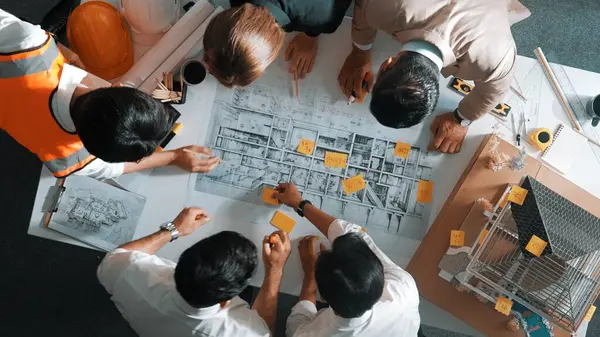 Top down view of skilled engineer team compare between blueprint and house plan. Aerial view of group of architect or designer discussing and point note to brainstorm about blueprint. Alimentation.