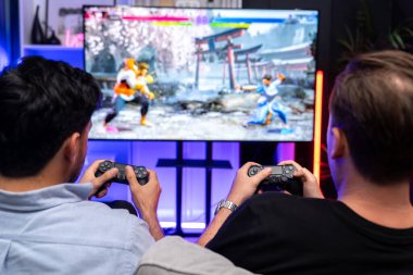 Oyun arkadaşları savaş sanatları dövüşçülerinin video oyununu arka plandaki joystickleri kullanarak oynuyorlar. Memlekette neşeli bir dövüşçüyle rahat bir neon ışığı. Satılabilir.
