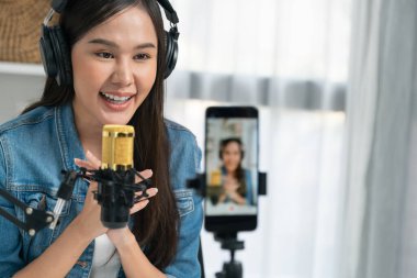 Asyalı sunucu canlı yayında canlı yayında canlı yayında sosyal medyada kulaklık takarak konuşuyor. Dinleyicileri modern stüdyoda koçluk yaparak selamlıyor. Taktik.