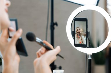 Sosyal medya için güzellik ve kozmetik video içeriği hazırlayan genç bir kadın. Güzellik blogcusu seyirciye güzellik hizmetini nasıl uygulayacağını ya da kamera karşısında takipçiyi nasıl izleyeceğini gösteriyor. Blithe