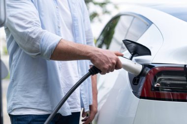 Çevre dostu bilinçli adam EV şarj istasyonundan modern elektrikli aracı şarj ediyor. EV araba teknolojisi gelecekteki sürdürülebilirlik için alternatif ulaşım aracı olarak kullanılıyor. Eşzamanlama