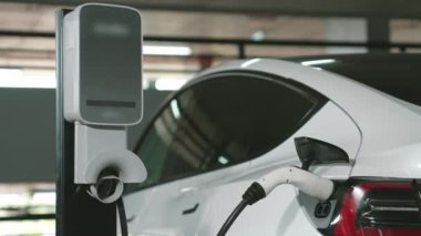 Şehir merkezindeki kapalı otoparkta yavaş çekimde EV elektrikli araba şarj oluyor. Şehir merkezinde sürdürülebilirlik yeşili, yeniden şarj edilebilir elektrikli araç iç organları.