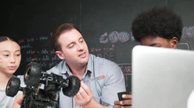 Akıllı öğretmen araba modelini farklı öğrencilere denetliyor. Melez ırk dinleyen liseli çocuklar masada dizüstü bilgisayarı ve kabloları olan robot model sistemini açıklıyor. Öğretim