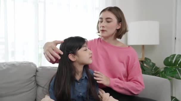 白人母亲抱着女儿 坐在沙发上亲吻额头 快乐的妈妈在客厅里向可爱的亚裔女学生示爱和爱心 可爱的家人花时间在一起 教育学 — 图库视频影像