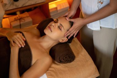 Beyaz kadın stres önleyici kafa masajı yapmaktan ve lüks otel veya otelde sıcak mum ışığında yüz güzelliği eğlencesi yapmaktan zevk alıyor. Sessiz.