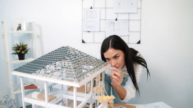 Young beautiful caucasian architect engineer turns house model around to inspect house construction and check mistake point to solve the problem on meeting table at modern office. Closeup. Immaculate. clipart