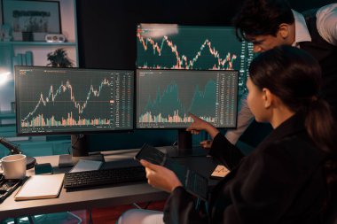 Dinamik döviz kuru risk yatırımı üzerine tartışan iki tüccar tablet üzerindeki verileri karşılaştırarak, gece neon ışıklı ofis odasındaki bilgisayar ekranlarının arka planına işaret ediyorlar. Varsayım.